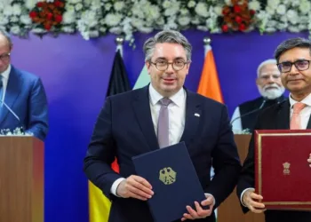 Indian and German officials exchange signed documents during a critical minerals agreement ceremony in January 2026, with PM Modi & Chancellor Friedrich Merz in the background