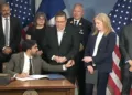 Mayor Mamdani asks Police Commissioner Jessica Tisch to pass the ceremonial 9/11 pen to his chief counsel Ramzi Kassem (extreme right)