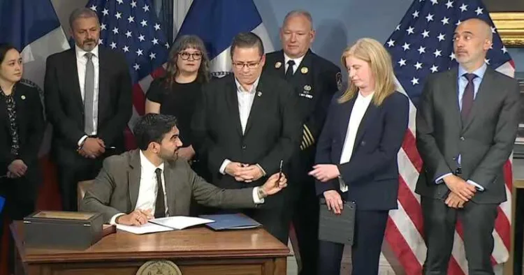 Mayor Mamdani asks Police Commissioner Jessica Tisch to pass the ceremonial 9/11 pen to his chief counsel Ramzi Kassem (extreme right)