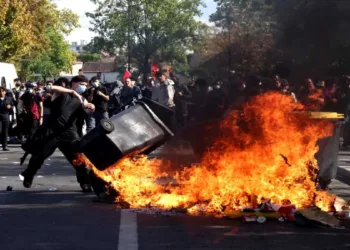 A masked protester throws a garbage bin into a burning pile of debris during clashes between the protesters and French riot police in Paris on October 8
