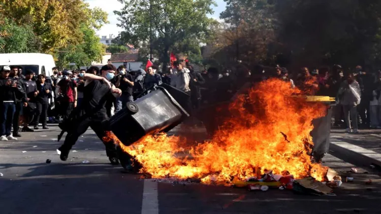 A masked protester throws a garbage bin into a burning pile of debris during clashes between the protesters and French riot police in Paris on October 8