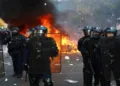 French riot police stand guard as flames and thick black smoke rise during violent street clashes, highlighting the escalating tensions surrounding student protests and public unrest