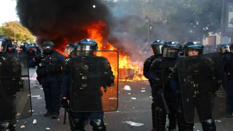 French riot police stand guard as flames and thick black smoke rise during violent street clashes, highlighting the escalating tensions surrounding student protests and public unrest